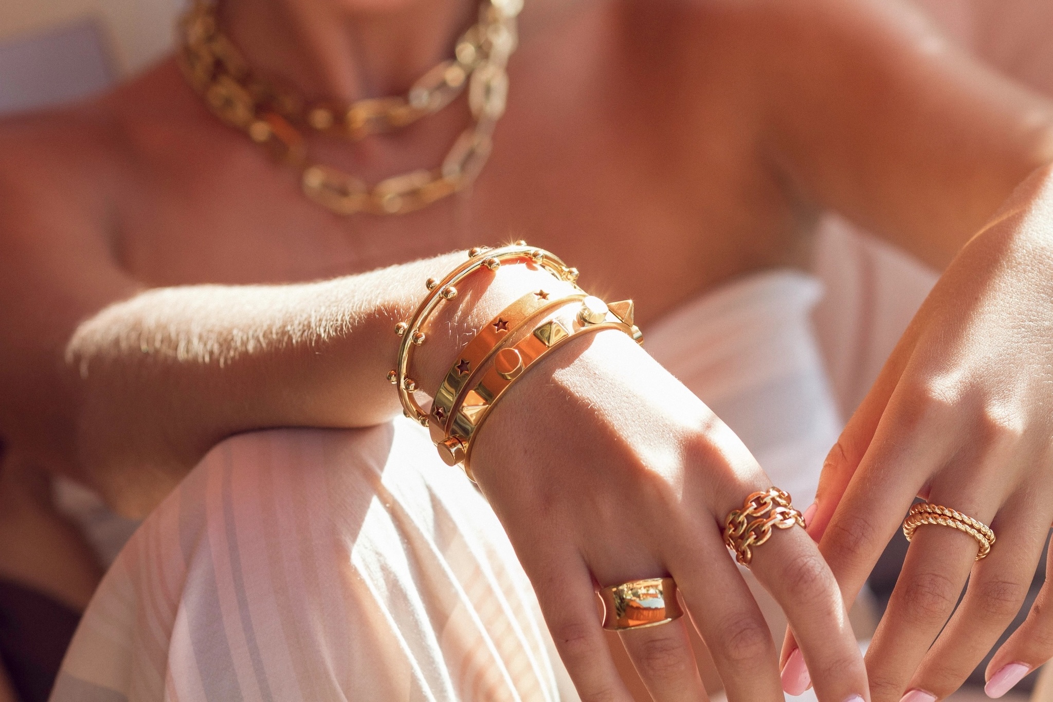 a closeup of golden bracelets and rings on a woman's hand